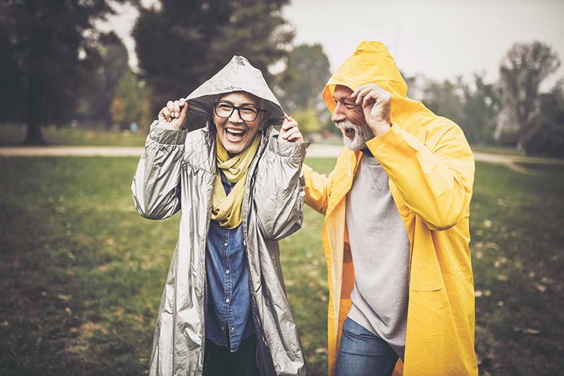 Dos jubilados con impermeables ríen mientras llueve